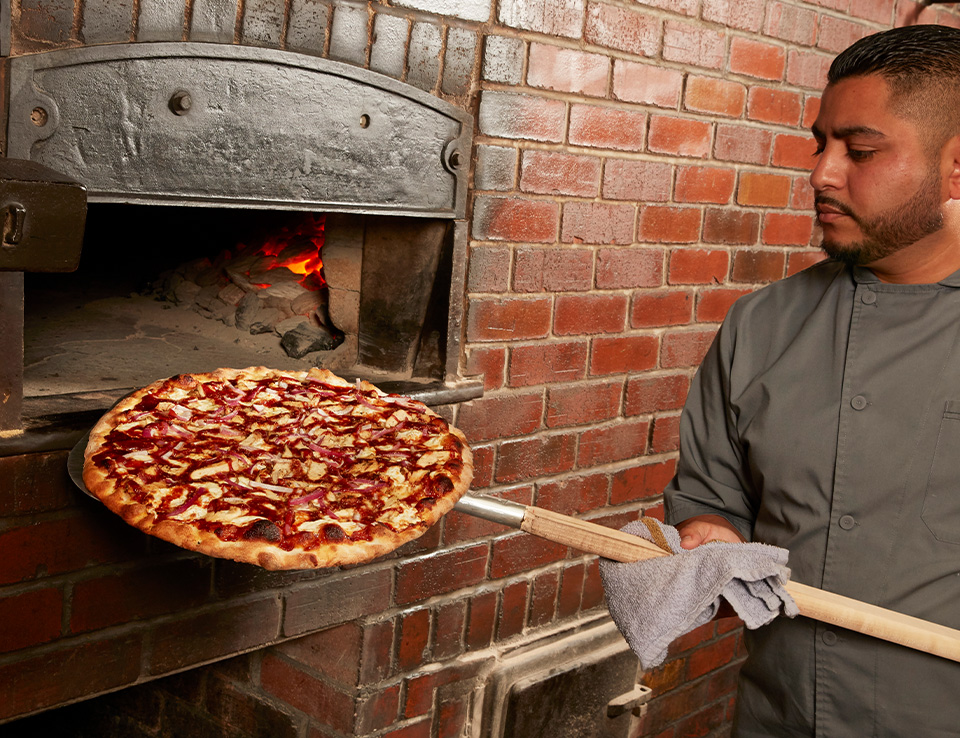 Grimaldi's employee putting pizza in pizza oven